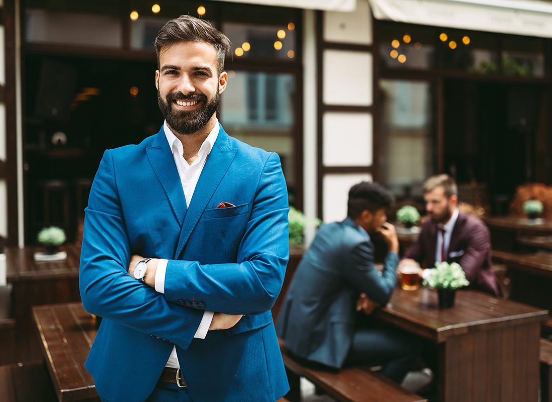 Business Insurance - Portrait of a Cheerful Young Business Owner Wearing a Suit with His Arms Folded While Standing Outside His Restaurant